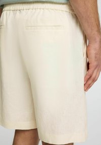 Krémové lněné šortky s elastickým pasem, které mají dvě zadní kapsy a hladký, texturovaný povrch.