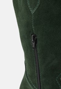 Bota de ante verde con una cremallera negra en el lateral, costura decorativa en un verde más claro y una textura suave.