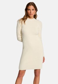 Abito maglione di colore crema con finitura testurizzata, maniche lunghe e scollatura alta. Presenta dettagli a bottone sulle spalle.