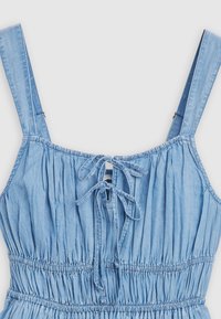 Απαλό μπλε τζιν φόρεμα με ρυθμιζόμενους ιμάντες, ριγωτή υφή και δέσιμο στο πίσω μέρος. Ελαστική ζώνη για προσαρμοσμένο σχήμα.