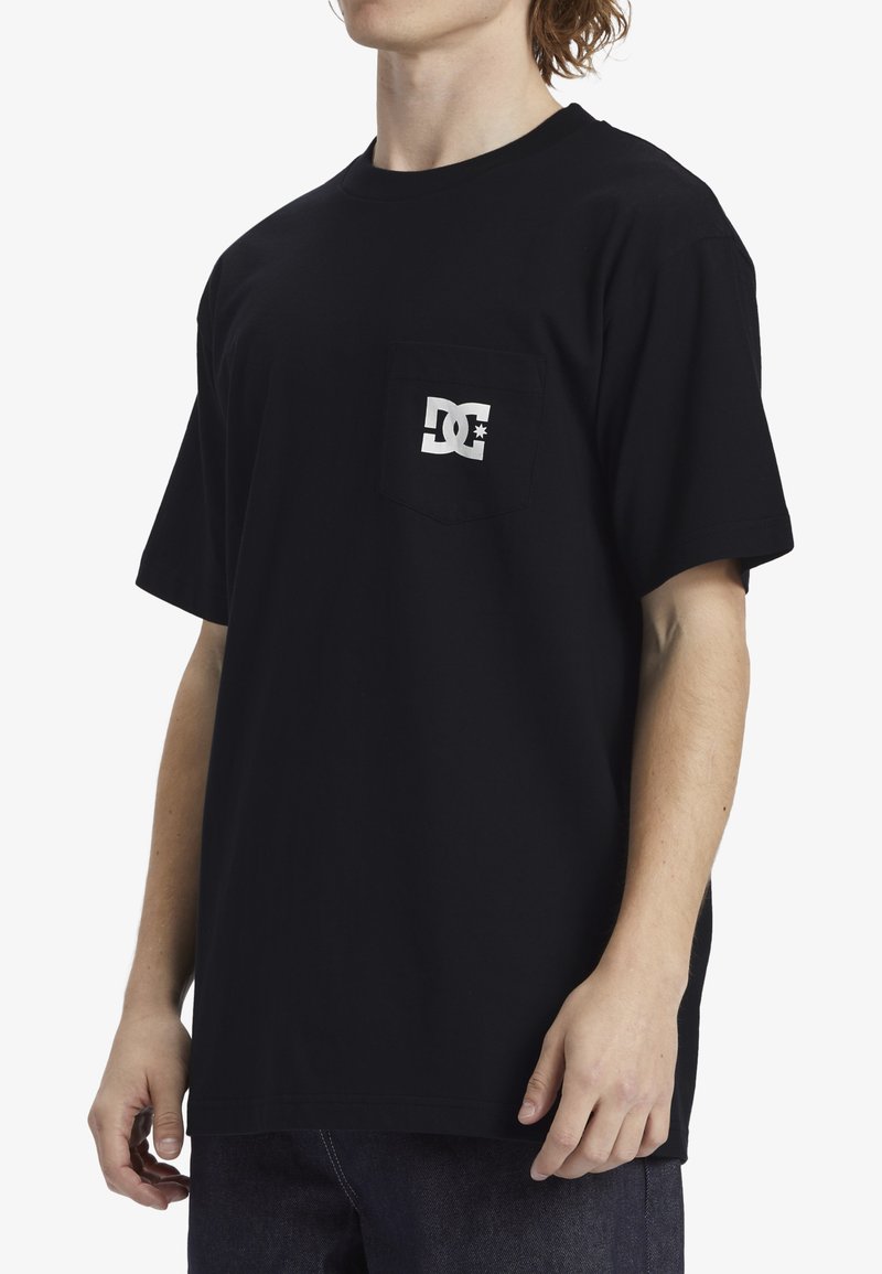T-shirt en coton noir à manches courtes, avec une poche sur la poitrine gauche, et un logo blanc contrastant imprimé sur la poche.