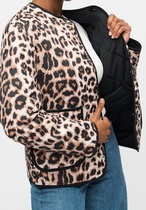 Person iført leopardprint jakke, der viser sort quiltet inderfor, kombineret med blå jeans og hvid top.