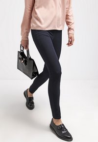 Musta nilkkapituinen slim-fit farkut, yhdistettynä vaaleanpunaiseen satiiniseen pitkähihapaitaan, mustiin loafereihin ja pieneen mustaan kiiltäväpintaiseen käsilaukkuun.