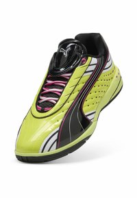 Scarpa sportiva verde lime e nera con materiale lucido in vernice, dettagli bianchi e rosa, superficie texturizzata e design perforato per la traspirabilità.