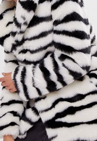 Plášť z umělé kožešiny s výraznými černobílými pruhy zebry, měkkou texturou a širokými rukávy, s mírně otevřeným designem límce.