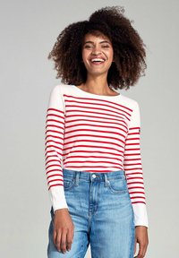 Chemise à manches longues rayée avec des rayures rouges sur fond blanc, décolleté rond et tissu doux, associée à un jean en denim bleu clair.