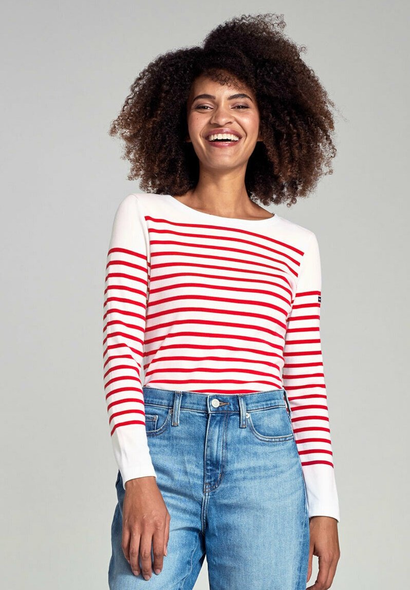 Chemise à manches longues rayée avec des rayures rouges sur fond blanc, décolleté rond et tissu doux, associée à un jean en denim bleu clair.