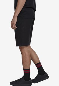 Shorts de sport noirs en mélange de coton, offrant une coupe décontractée. Associés à des chaussures noires et des chaussettes noires avec des rayures rouges et vertes.