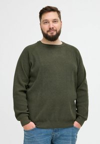 Pull en tricot vert à manches longues, col rond, et en tissu texturé. Associé à un jean en denim bleu.