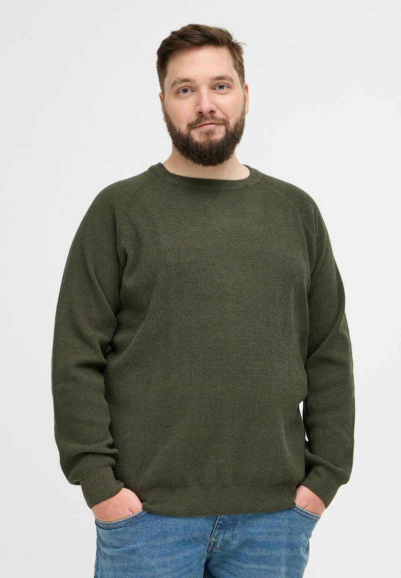 Pull en tricot vert à manches longues, col rond, et en tissu texturé. Associé à un jean en denim bleu.