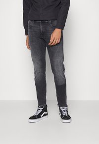 Jeans de mezclilla oscuros de corte ajustado con un aspecto desgastado, combinados con zapatillas altas negras con acentos y cordones blancos.