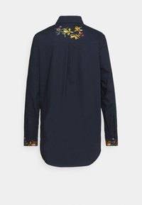 Chemise bleu marine à manches longues avec broderie florale sur le haut du dos et les poignets, avec un pli au centre du dos.