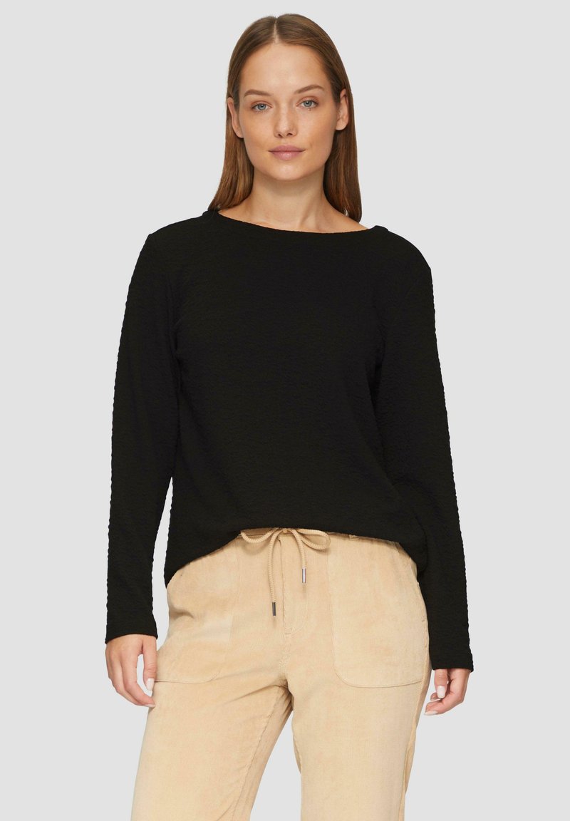 Haut noir à manches longues avec une finition texturée, un col large et une coupe décontractée, associé à un pantalon en velours côtelé beige clair avec une taille à cordon.