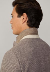 Veste à carreaux bruns avec un col montant, fabriquée en mélange de laine texturé et dotée d'une bordure de col plus claire. Coupe ajustée avec des coutures définies.