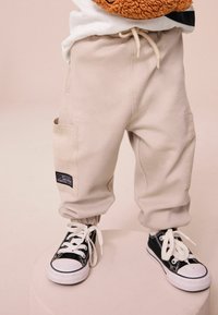 Beige cargobyxor med elastiska muddar, sidofickor och dragsko i midjan, kombinerat med svarta sneakers med vita snörningar och tåhätta.