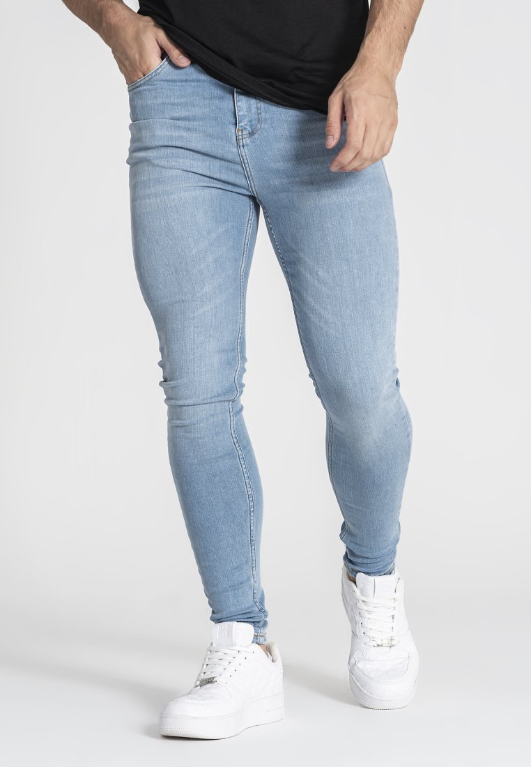 Jeans ajustados de mezclilla de color azul claro, con un corte ceñido, un leve desvanecimiento y una cintura de altura media, combinados con zapatillas blancas.