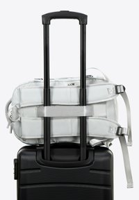 Valise noire à roulettes avec un sac à dos argenté fixé sur le dessus, comportant des sangles réglables et des zippers, ainsi qu'une poignée lisse.