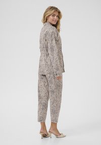 Traje de estampado de leopardo en tonos beige y negro, que incluye una chaqueta entallada con cuello y pantalones ajustados a juego, confeccionados en una tela suave.