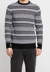 Czarnobiały sweter z wzorem w geometryczne kształty, z okrągłym dekoltem, ściągaczami na mankietach i u dołu. Wykonany z dzianiny.