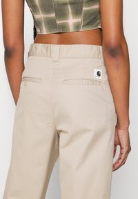 Personne portant un pantalon beige Carhartt et un top court vert tie-dye, vue de dos.