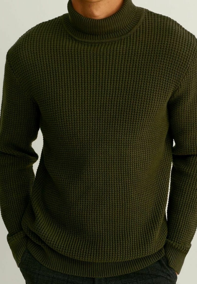 Pull en maille vert olive avec un col montant côtelé, un motif texturé et des poignets ajustés, conçu pour la chaleur et le confort.