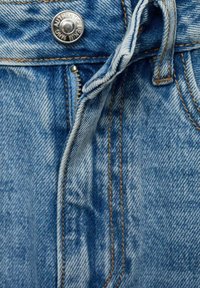 Modre denim hlače z vidnim zadrgo, srebrnim gumbom in detajli iz oranžnega šivanja. Tkanina ima teksturiran zaključek z zbledelim videzom.