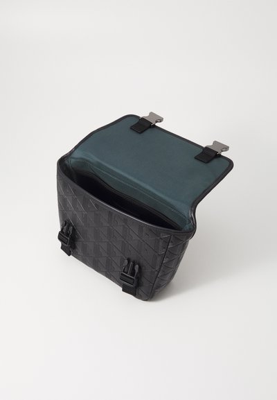 Sac noir texturé avec un motif géométrique, ouvert pour révéler un intérieur vert. Comprend des accessoires en métal et des sangles ajustables.