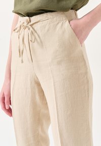 Beige Leinenhosen mit lockerer Passform, elastischem Bund und Seitentaschen. Der Stoff hat eine subtile Textur und leichte Falten.