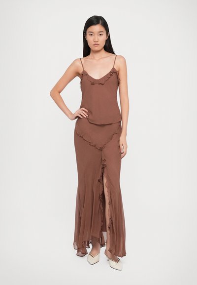 Brown two-piece outfit with ruffled trim. The top features thin straps, while the long skirt has a slit and ruffles along the hem.