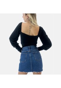 Top nero a maniche lunghe con scollatura quadrata, abbinato a una mini gonna di denim con orlo sfrangiato e due tasche posteriori.