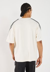 Chemise à manches courtes couleur crème avec des rayures noires sur les côtés, fabriquée en tissu doux, présentant une coupe décontractée et un col rond.