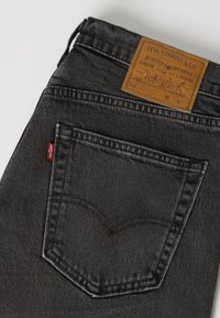 Μαύρο τζιν Levi's που δείχνει πίσω τσέπη με κόκκινη ετικέτα Levi's και καφέ δερμάτινο λογότυπο πάνω από τη μέση.