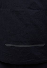 Marineblauer Stoff mit einer strukturierten Oberfläche. Verfügt über einen reflektierenden horizontalen Streifen in der Nähe des Bodens. Einfaches Design, keine sichtbaren Verschlüsse oder Muster.