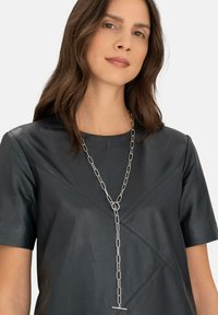 Sort læder top med korte ærmer, præget af diagonale syninger, suppleret med en sølvkæde med langstrakte led og en toggle clasp.