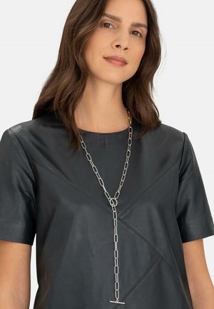 Schwarzes Lederoberteil mit kurzen Ärmeln und diagonaler Naht, ergänzt durch eine silberne Kettenhalskette mit länglichen Gliedern und einem Toggle-Verschluss.