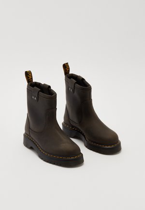 Bruine leren enkellaarsjes met afgeronde neuzen, gele stiksels en zwarte rubberen zolen. Voorzien van trekbanden voor gemakkelijk dragen. Soepele textuur.