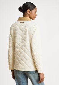 Jachetă crem matlasată cu guler din corduroi maro deschis, având cusături în formă de diamant și croială dreaptă și elegantă.