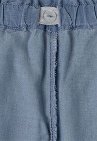 Tejido azul claro con una cinturilla recogida, que presenta una costura central y un cierre de botón. Textura suave y lisa con algunos bordes deshilachados.