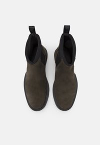 Bottes chelsea en suède marron avec un panneau latéral élastique noir, bout rond et une languette pour un enfilage facile. Semelle en caoutchouc plate.