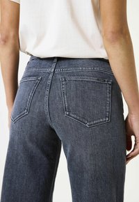 Donkergrijze spijkerbroek met een smalle taille, rechte pijpen en achterzakken met contrasterende stiksels en een subtiele textuur.