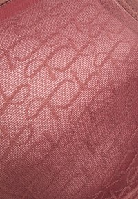 Texturovaná tkanina v rôznych odtieňoch ružovej s jemným geometrickým vzorom, ktorá má hladký, mäkký povrch a ľahký lesk.