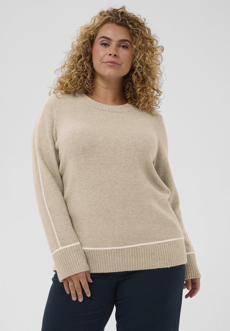 Pull en maille beige avec ourlet et poignets côtelés, présentant des lignes d'accent blanches le long des côtés. Matière douce et texturée.