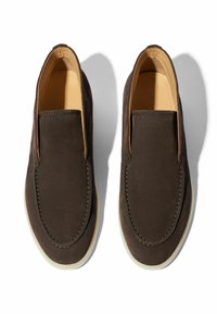 Zapatos slip-on de ante marrón con un acabado suave, puntera redondeada y suela de goma blanca. Costuras sutiles a lo largo de los bordes.
