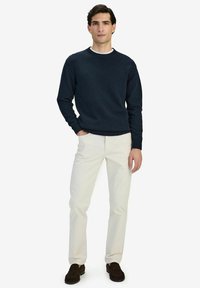 Marinblått stickat tröja med rund halsringning, ribbade ärmslut och nederkant, i kombination med krämfärgade byxor och bruna skor. Enkel, klassisk design.