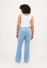Light blue flared jeans made of denim with a back pocket design. Worn with a white tank top, showcasing a simple and clean silhouette.