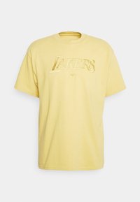 Camiseta amarilla de manga corta de Nike con logo de texto "LAKERS" en dorado en el pecho, cuello redondo y corte holgado.