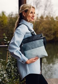 Zweifarbige Tasche mit einem dunklen oberen Teil und einem hellblauen unteren Teil, gefertigt aus strukturiertem Kunstleder, mit einem Reißverschlussfach und einem verstellbaren Tragegurt.