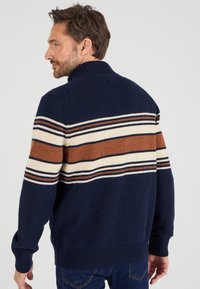 Pull de marine avec un col haut, orné de rayures horizontales crème, marron et marine. Texture tricotée avec des poignets et un ourlet côtelés.