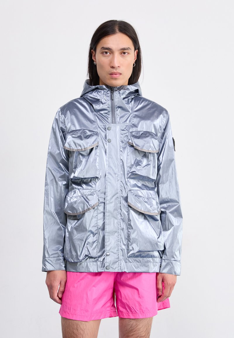 Silver reflective jacket with a hood, four front pockets, and grey trim. Paired with bright pink shorts. Smooth texture. Casual design.