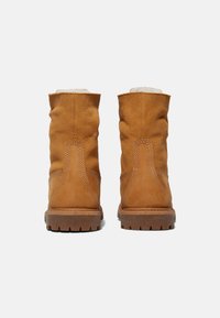 Bottines en daim marron avec une finition texturée, un haut arrondi, des coutures visibles et une semelle en caoutchouc robuste. Conçues pour le confort et la durabilité.